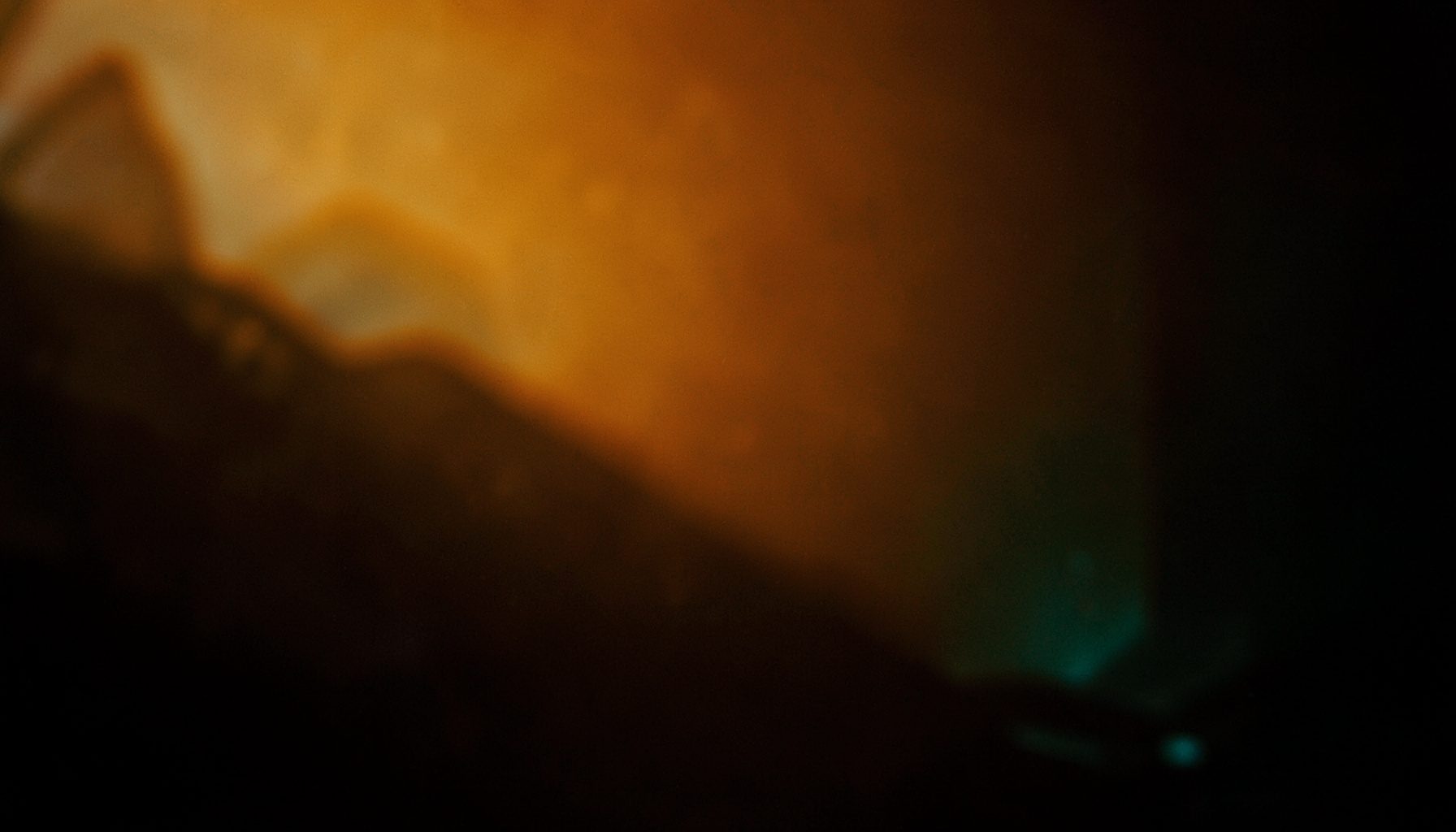 Golden amber light with soft teal shadows in a warm, intimate dark space
